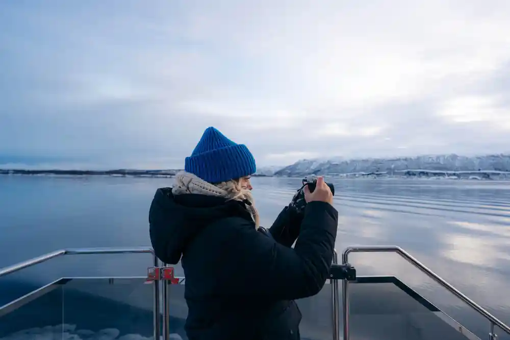 Woman on boat deck photographing snow-covered mountains